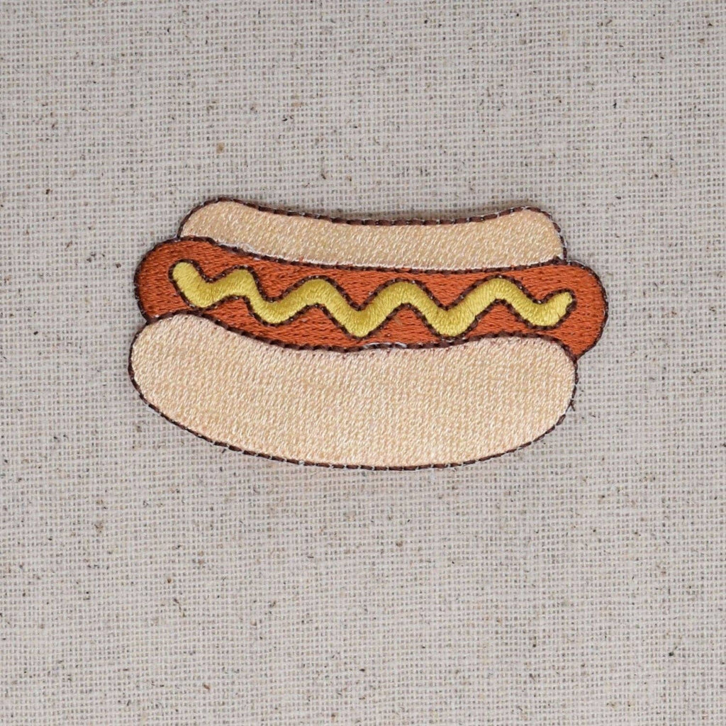 Embroidered patch of a hot dog with mustard on a textured fabric background
