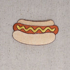 Embroidered patch of a hot dog with mustard on a textured fabric background