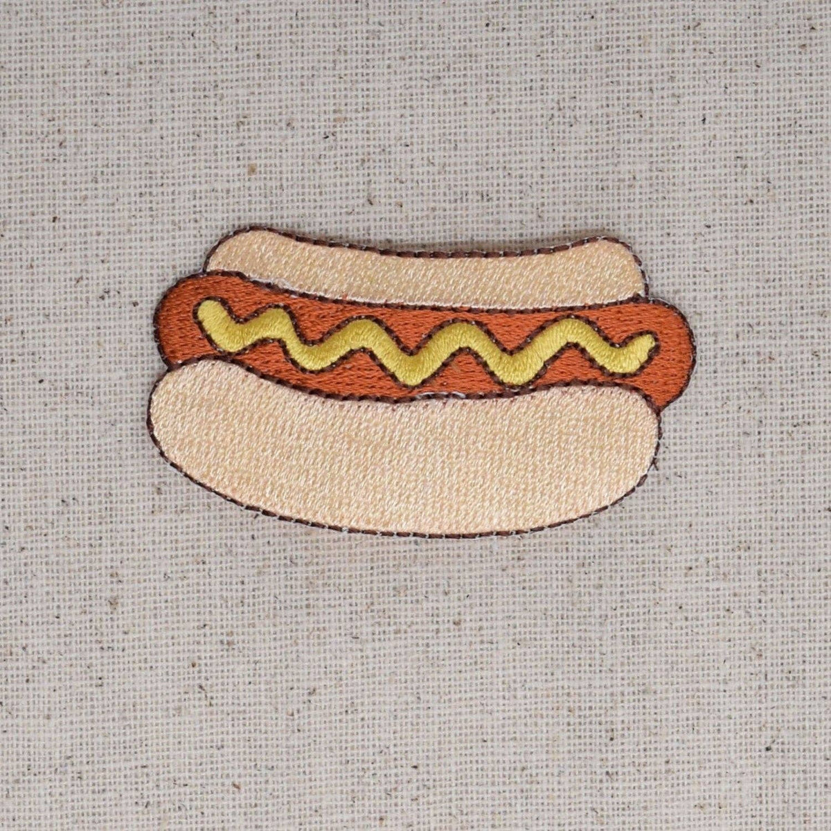 Embroidered patch of a hot dog with mustard on a textured fabric background
