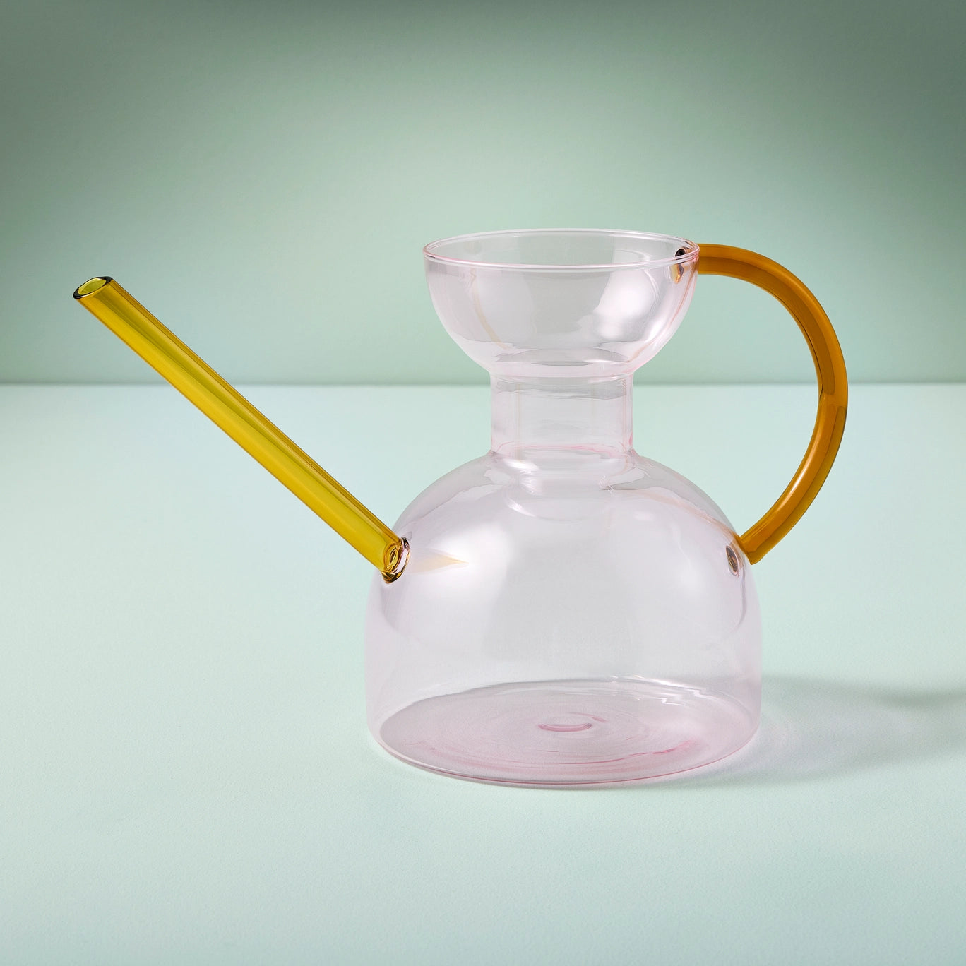 Pink Clear glass pitcher with yellow spout and handle on a light green background