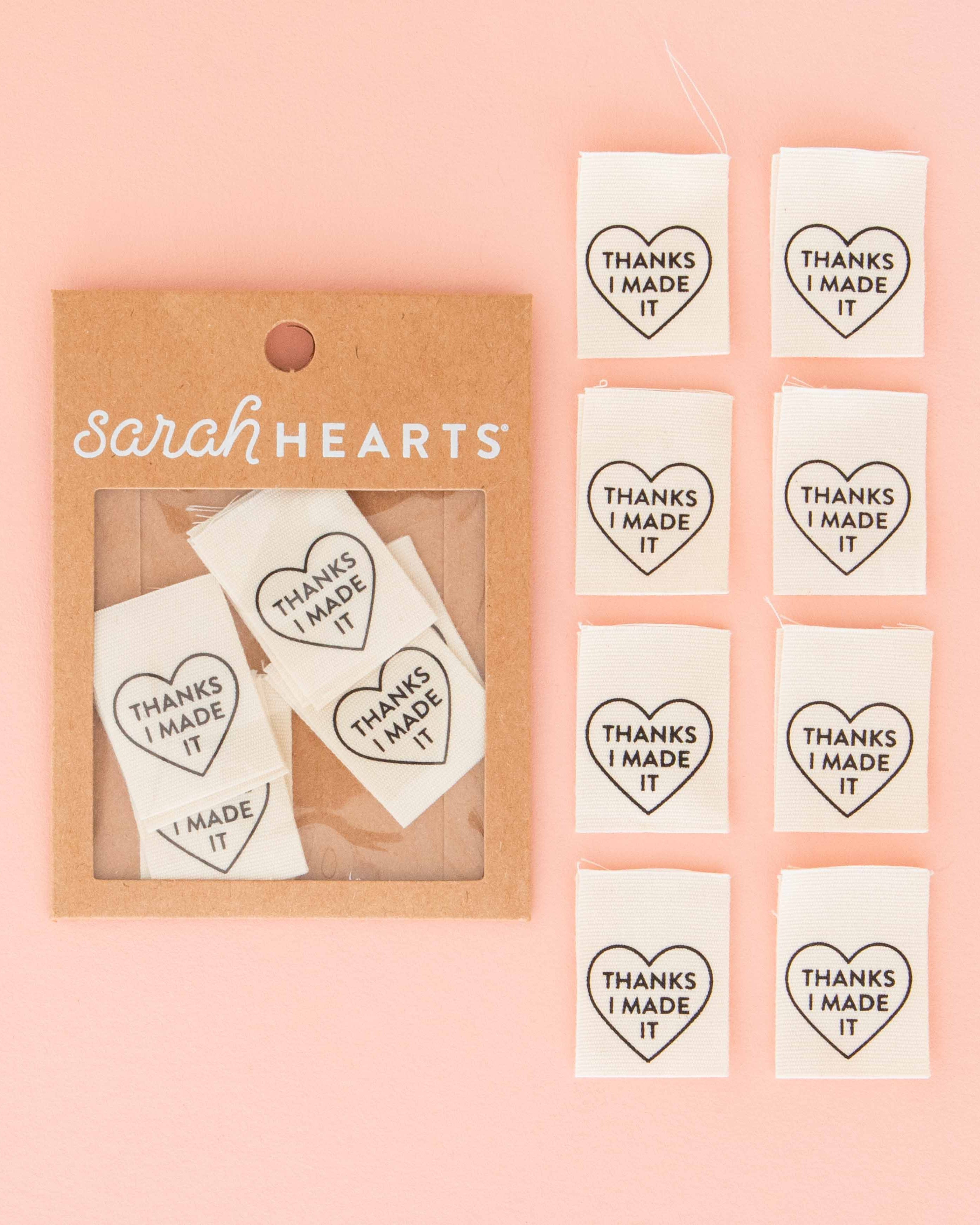 Heart-shaped sew-in labels with 'Thanks I Made It' text in a 'Sarah Hearts' packaging on a pink background