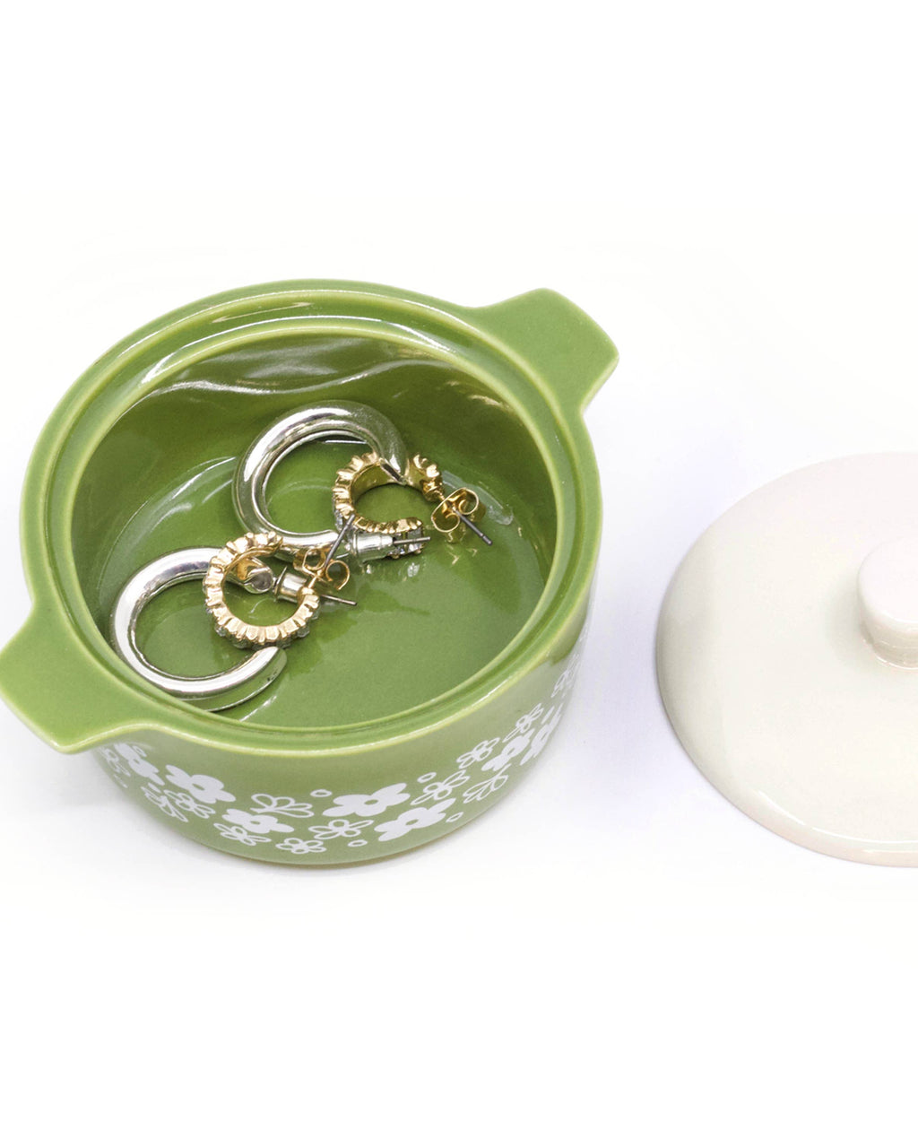 A small green ceramic trinket box with a white floral pattern, shown open with two metal rings inside, alongside its off-white lid on a white background.