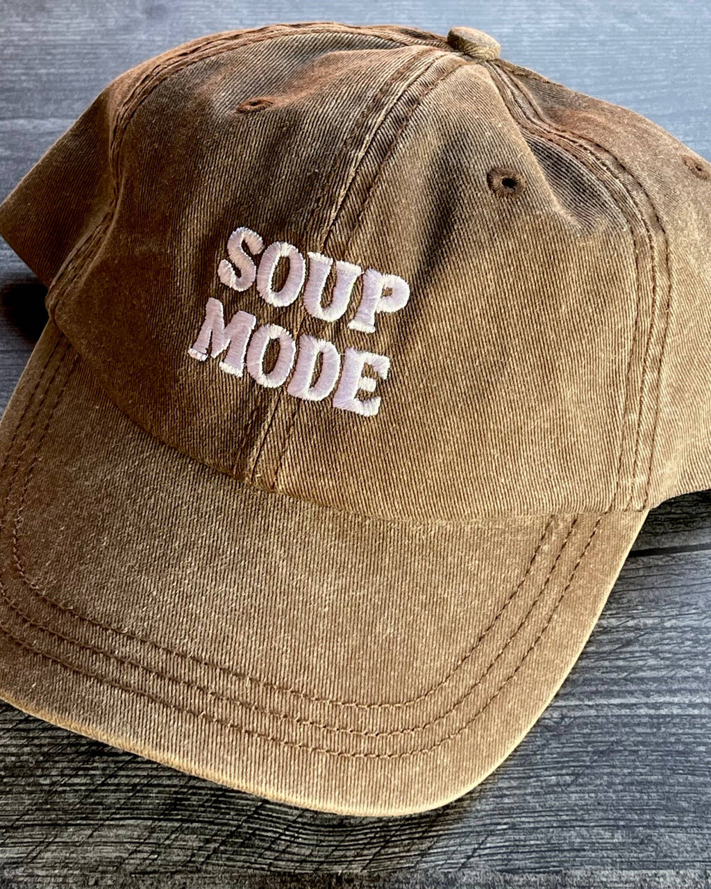 Brown cap with 'SOUP MODE' text on a wooden surface