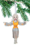 Decorative ornament of Dolly Parton in a silver dress with orange accents hanging from a branch.