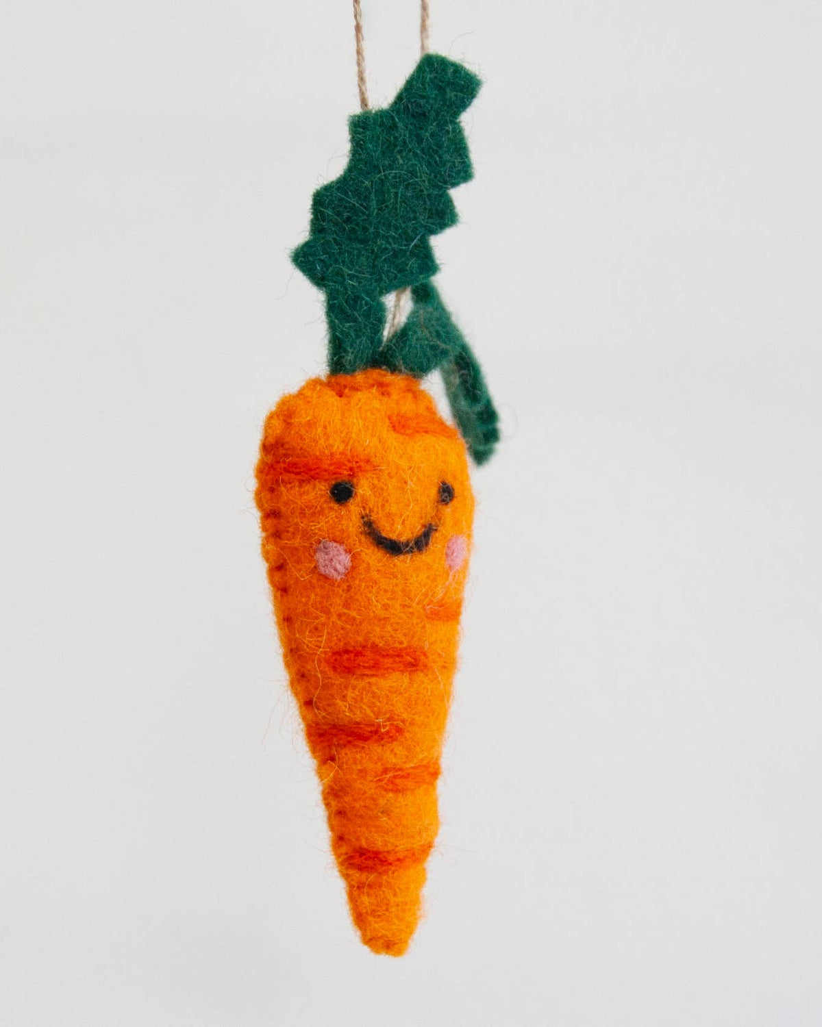 A handmade orange felt carrot ornament with a smiling face, pink cheeks, and a dark green felt leafy top, hanging against a plain white background.