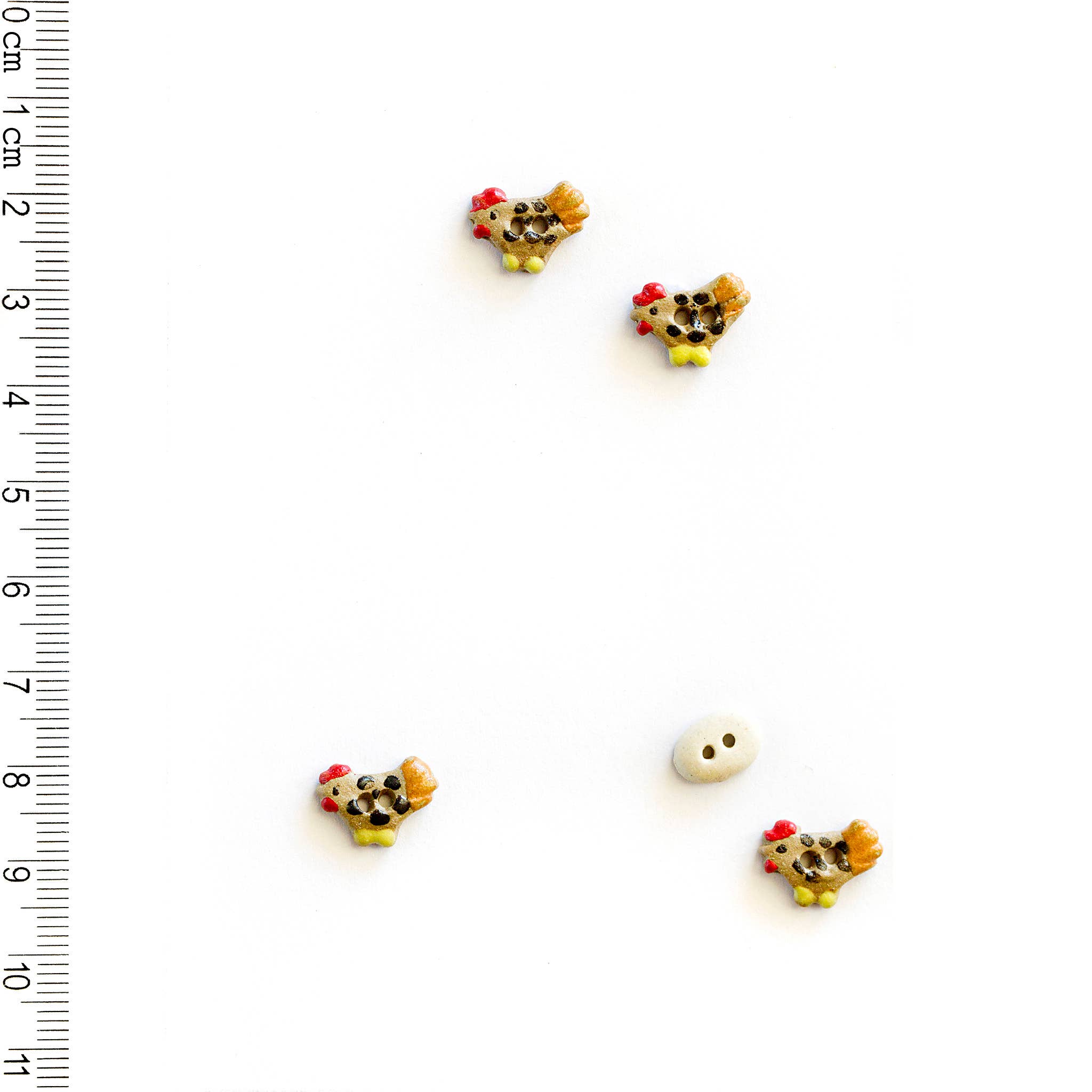 Four small decorative chicken buttons and one small white egg button with a ruler for scale on a white background