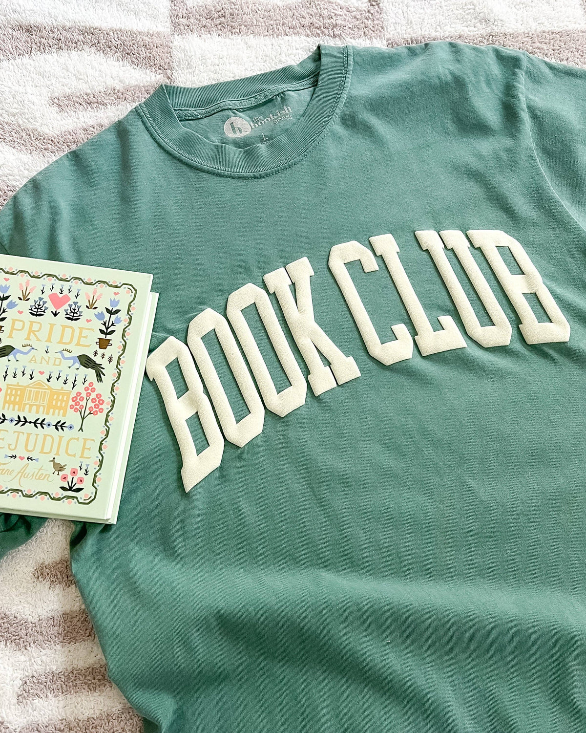 Green t-shirt with 'BOOK CLUB' text and a book on a striped fabric background