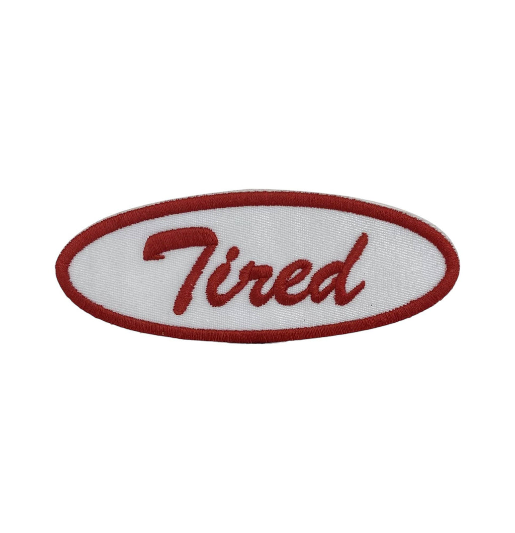 Red and white embroidered patch with 'Tired' text on a white background