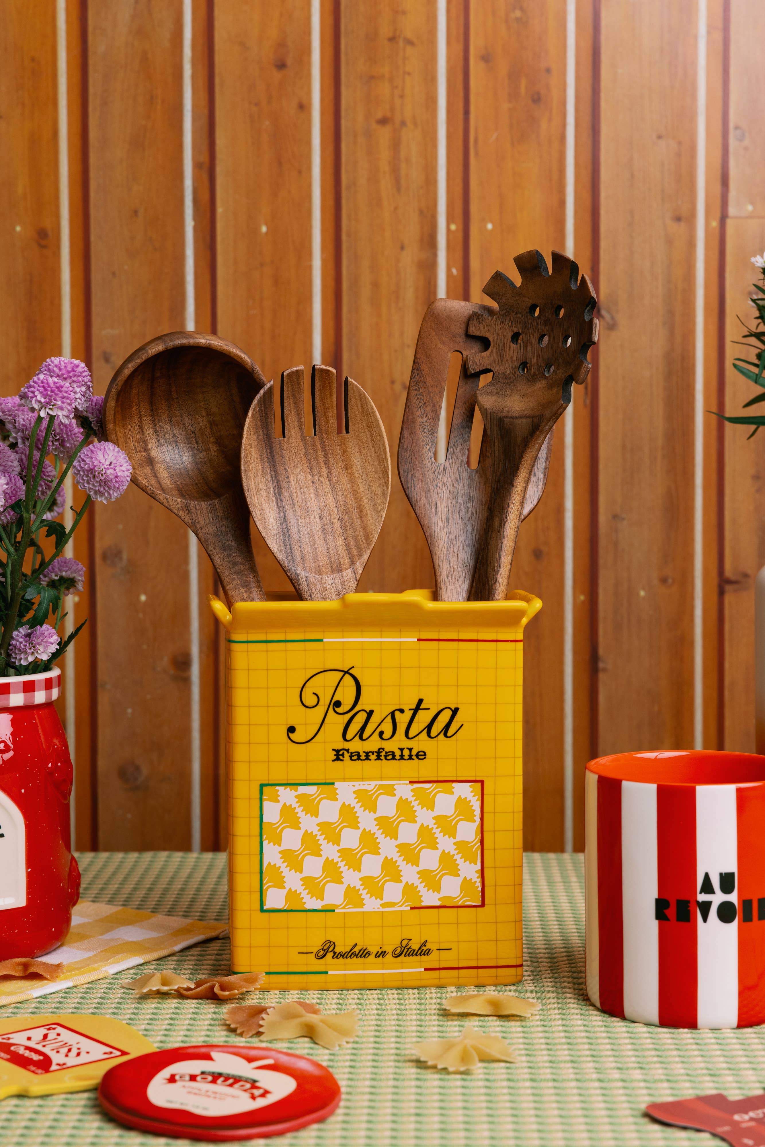 Yellow pasta container with wooden utensils on a table with a wooden wall background
