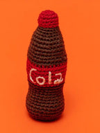 Crocheted Cola bottle shaped dog toy on an orange background