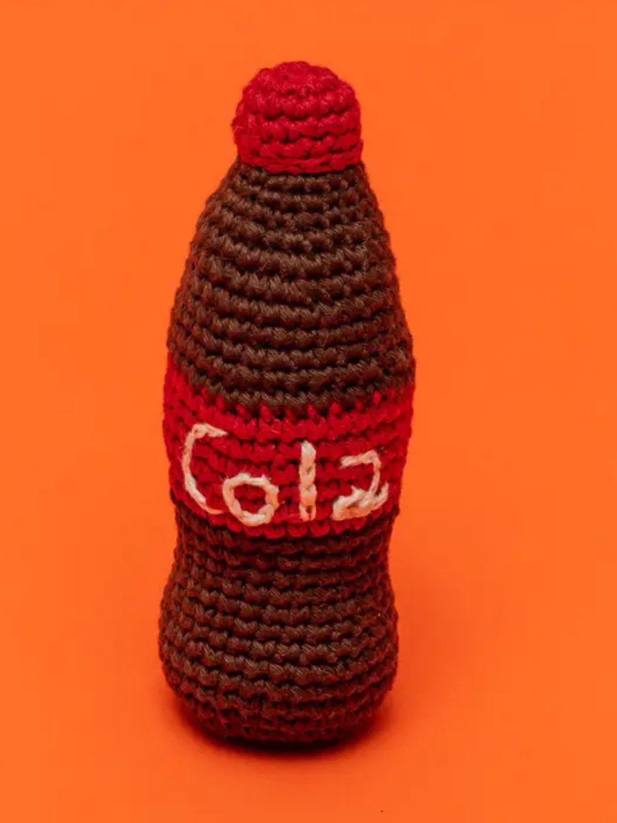 Crocheted Cola bottle shaped dog toy on an orange background