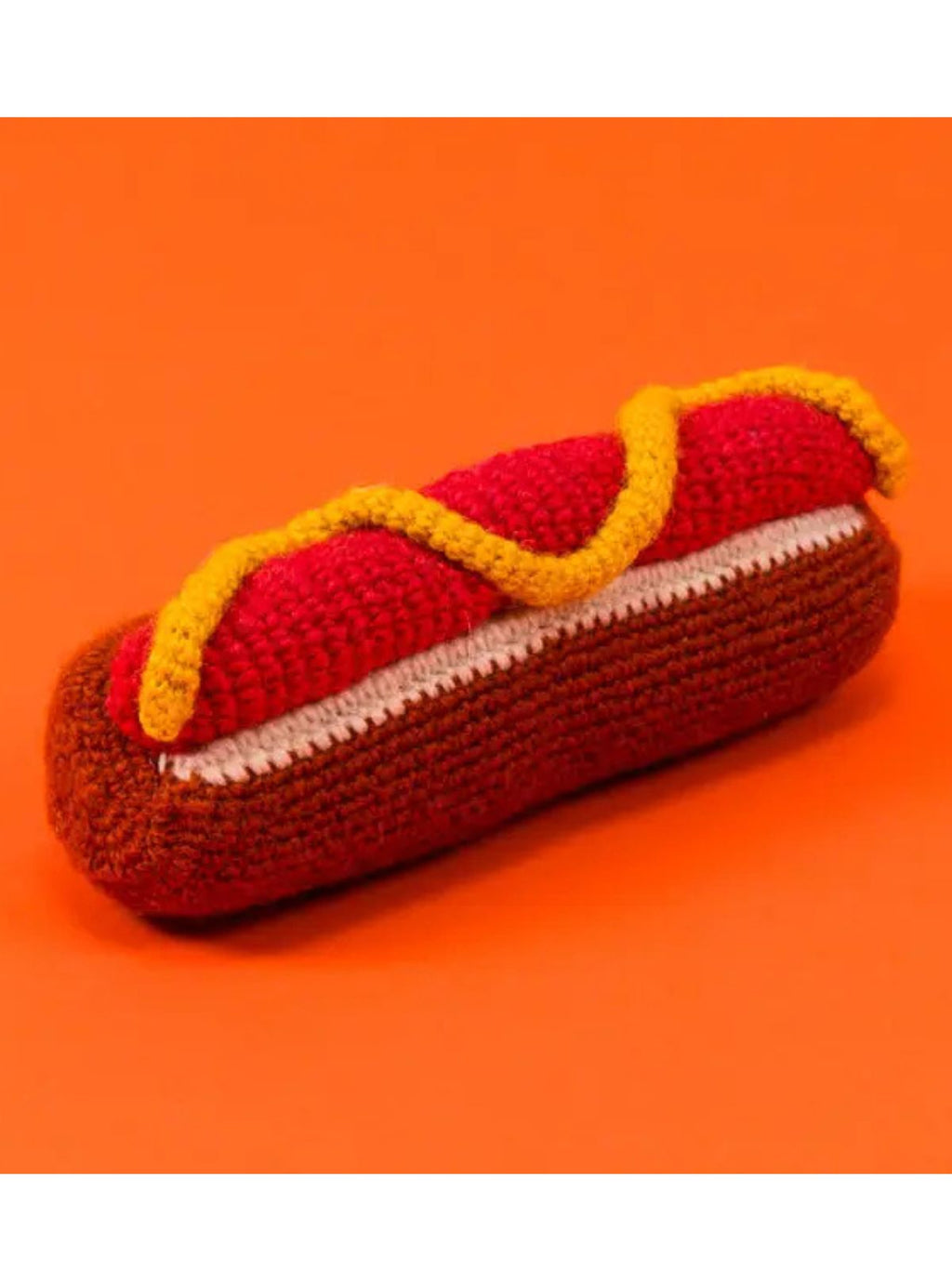 Crocheted hot dog toy with a bun on an orange background