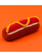 Crocheted hot dog toy with a bun on an orange background