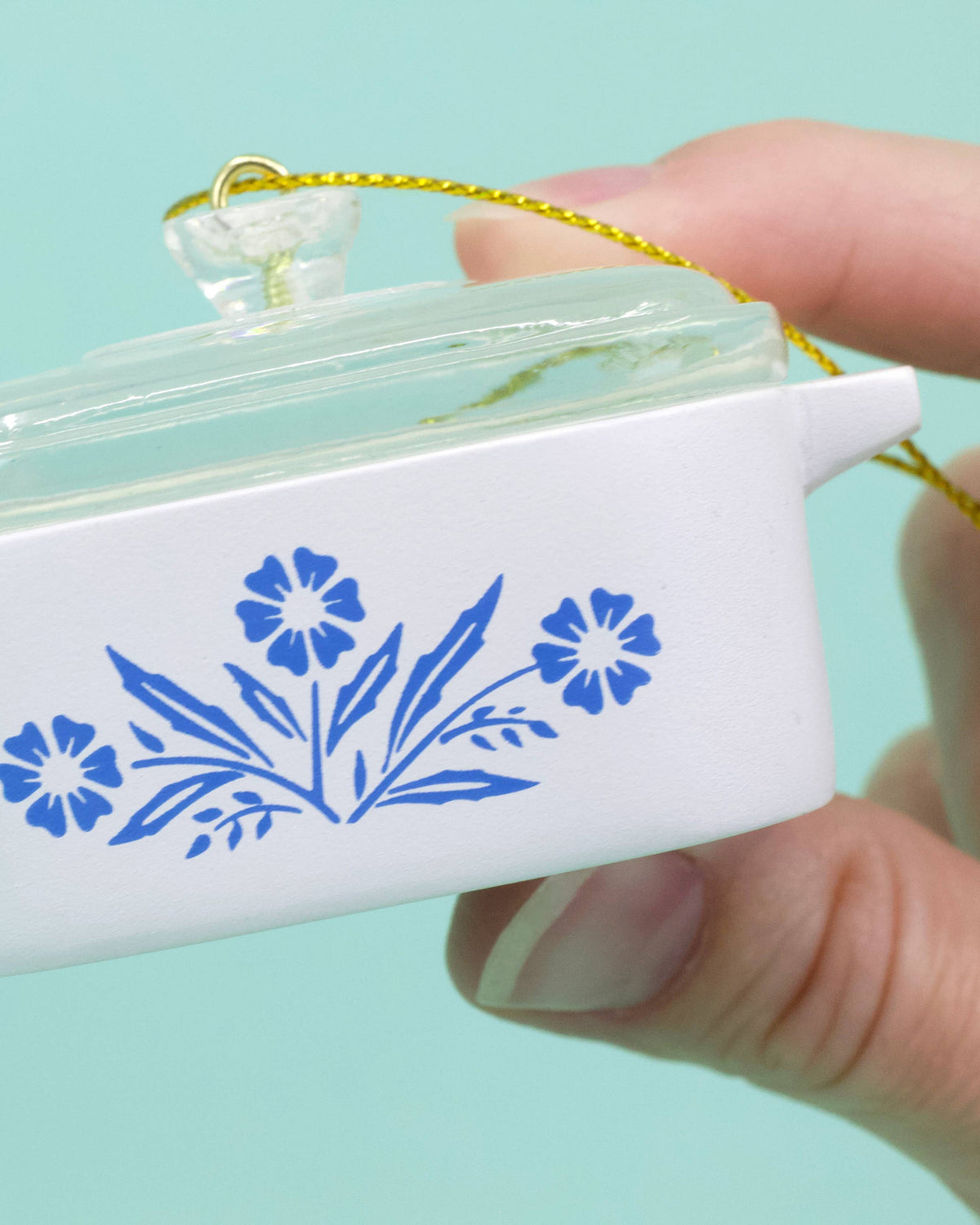 Small white ornament with blue floral design held by a hand against a light blue background