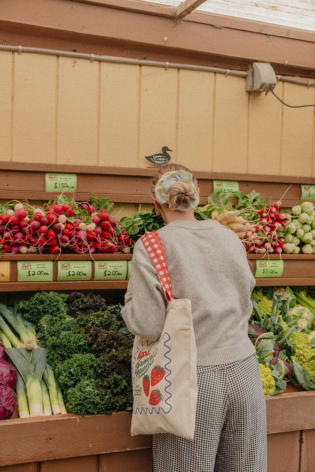 Person shopping at a farmers market wearing a blue and yellow scrunchie with a reusable bag.