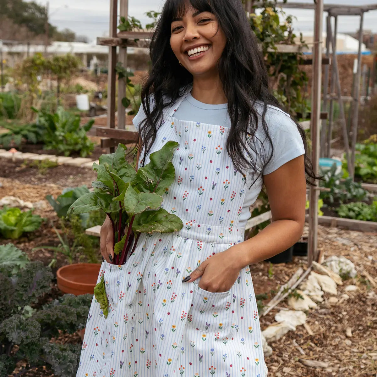 Woman holding leafy greens in a garden in a floral pattern apron