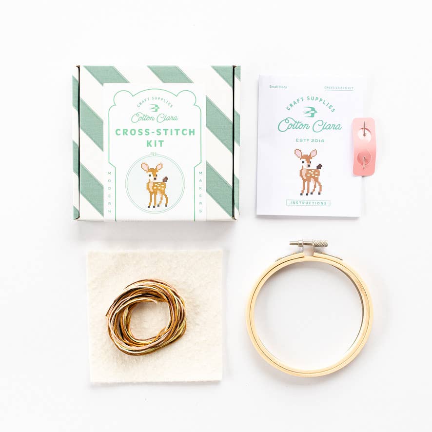 Cross-stitch kit with a box, thread, and hoop on a white background