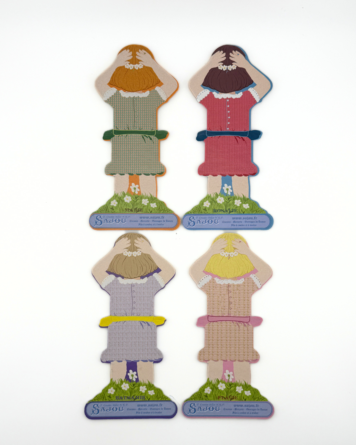 Back of four paper doll thread storage with different dresses on a white background