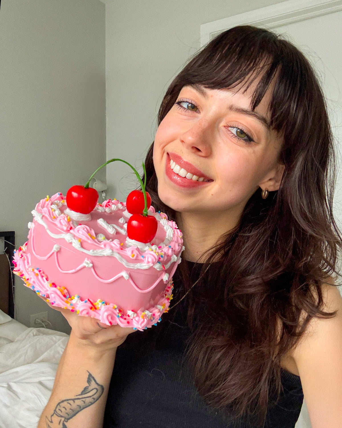 Woman holding a fake pink cake with cherries and sprinkles indoors.