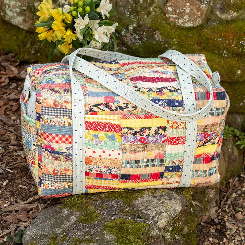 Colorful patchwork bag with white handle on a stone surface with flowers in the background
