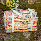 Colorful patchwork bag with white handle on a stone surface with flowers in the background