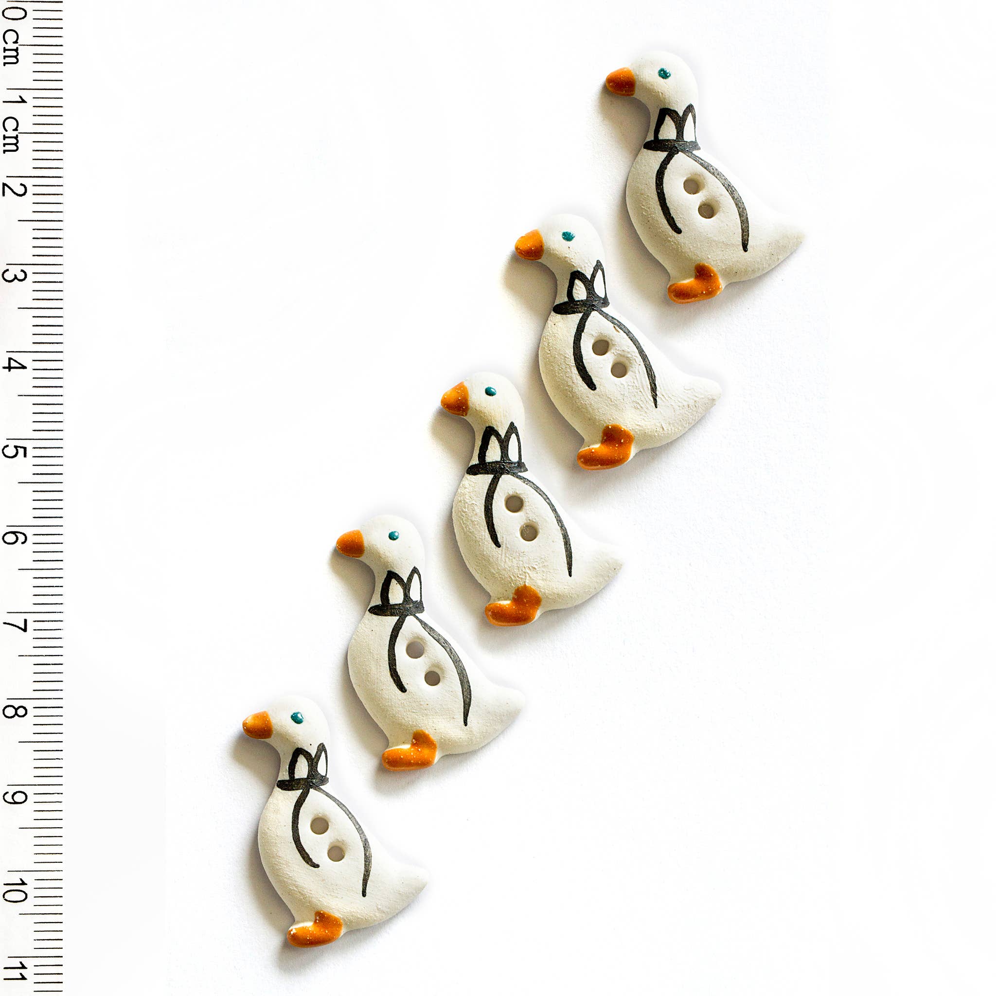 Set of five goose-shaped buttons with a ruler for scale on a white background