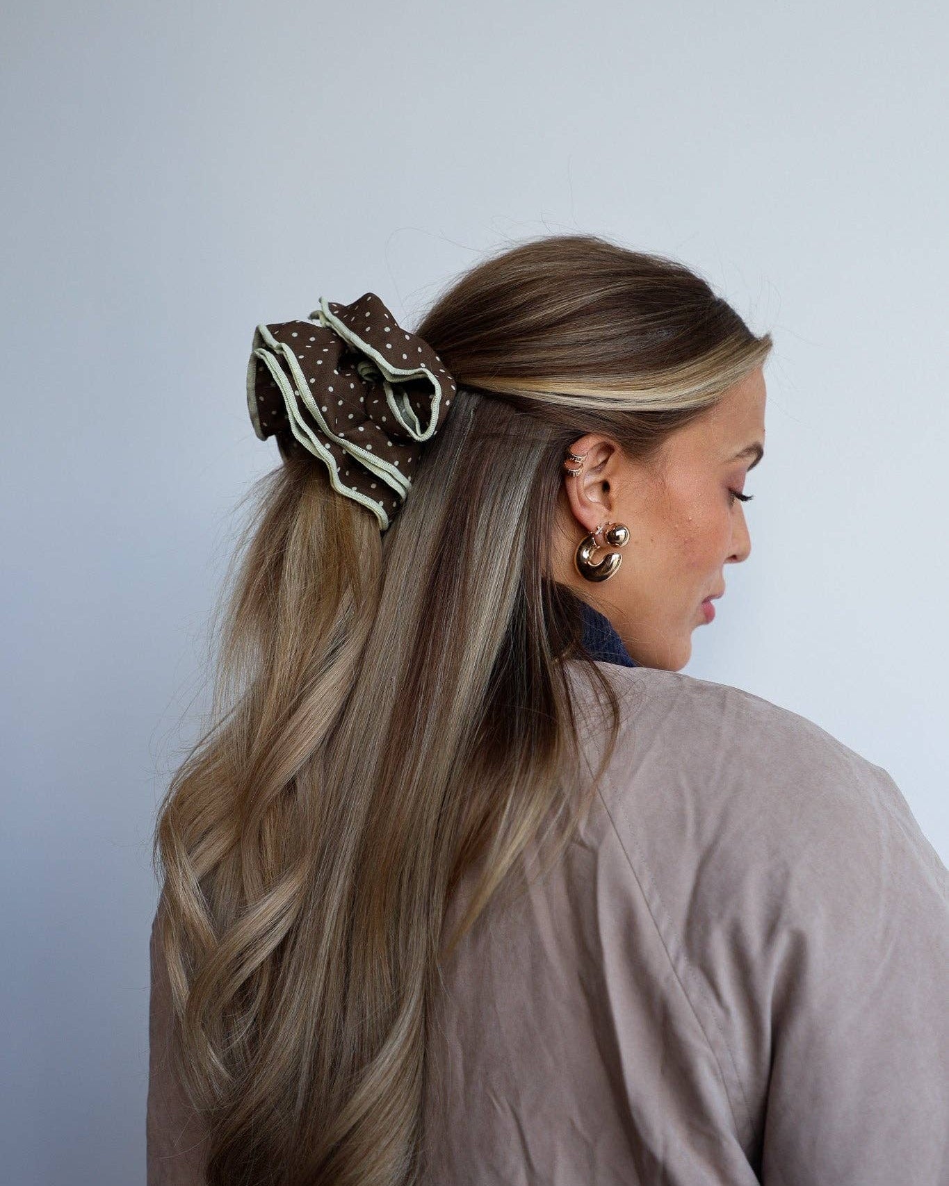 Woman with long blonde hair wearing a decorative black and white hair scrunchie against a plain background
