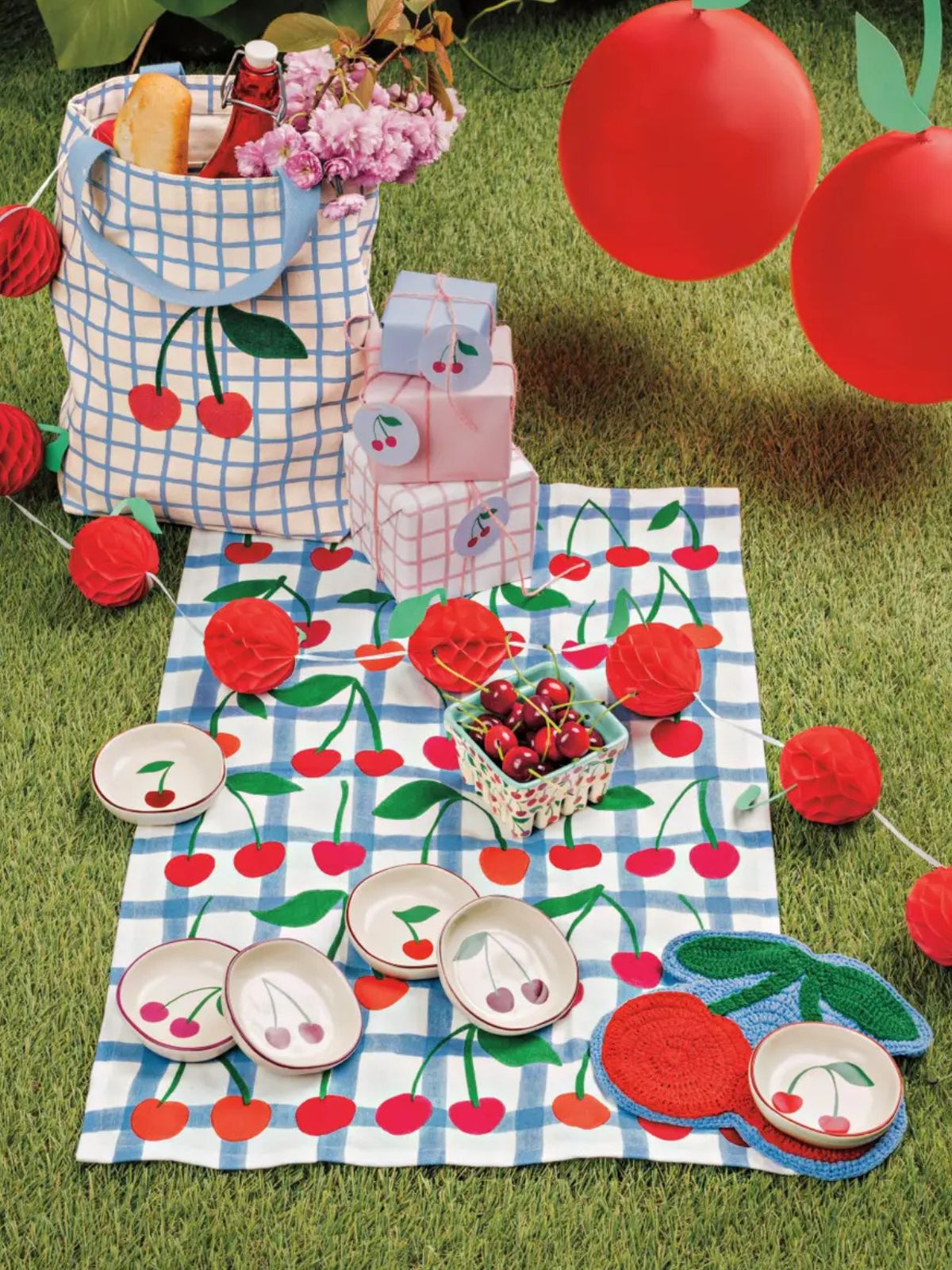 Picnic setup with cherry-themed tablecloth, plates, and basket on grass