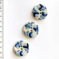 Three blue floral-patterned buttons with blue flowers on a white background, accompanied by a ruler for scale.