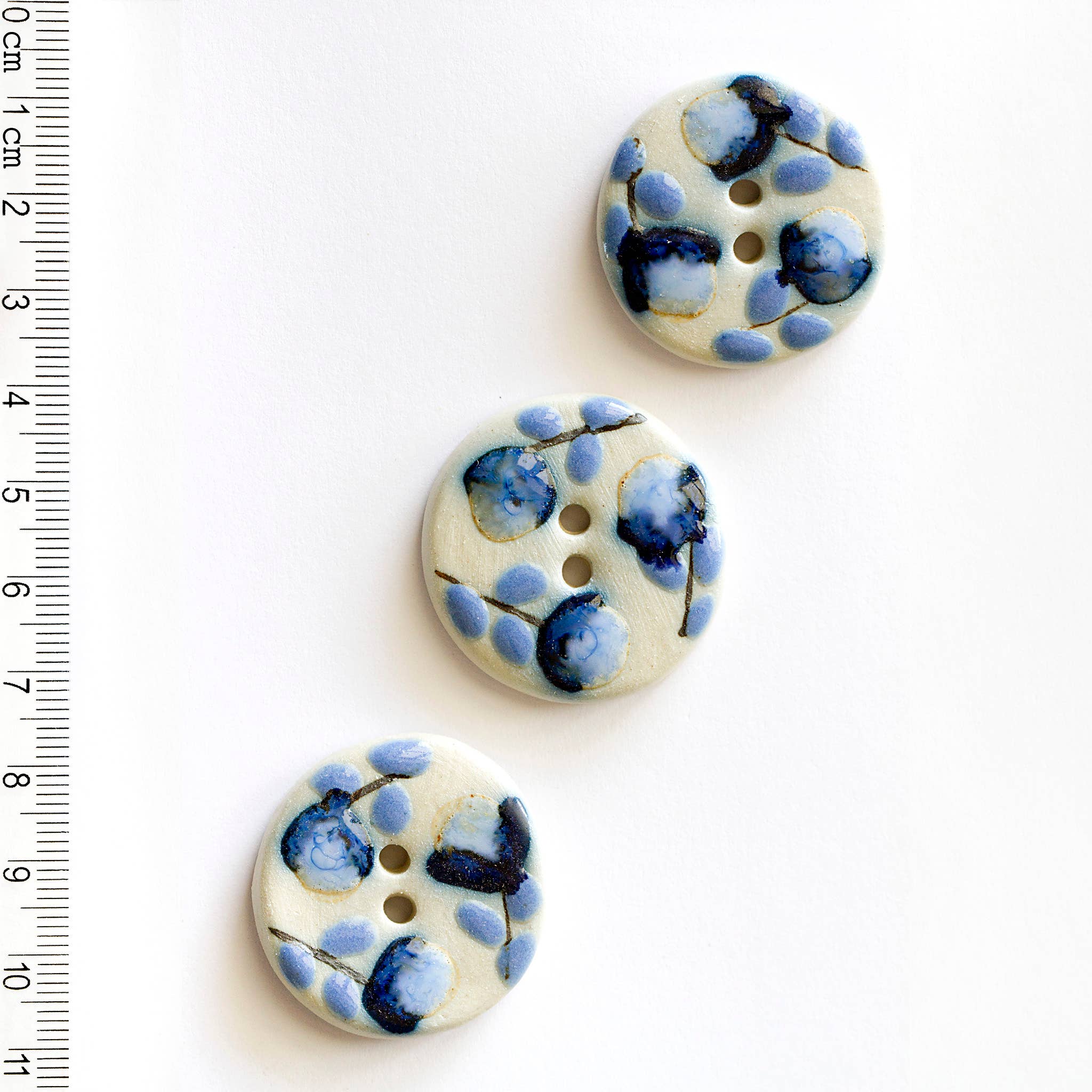 Three blue floral-patterned buttons with blue flowers on a white background, accompanied by a ruler for scale.