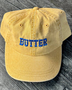 Pastel yellow cap with 'BUTTER' embroidered in blue on a wooden surface
