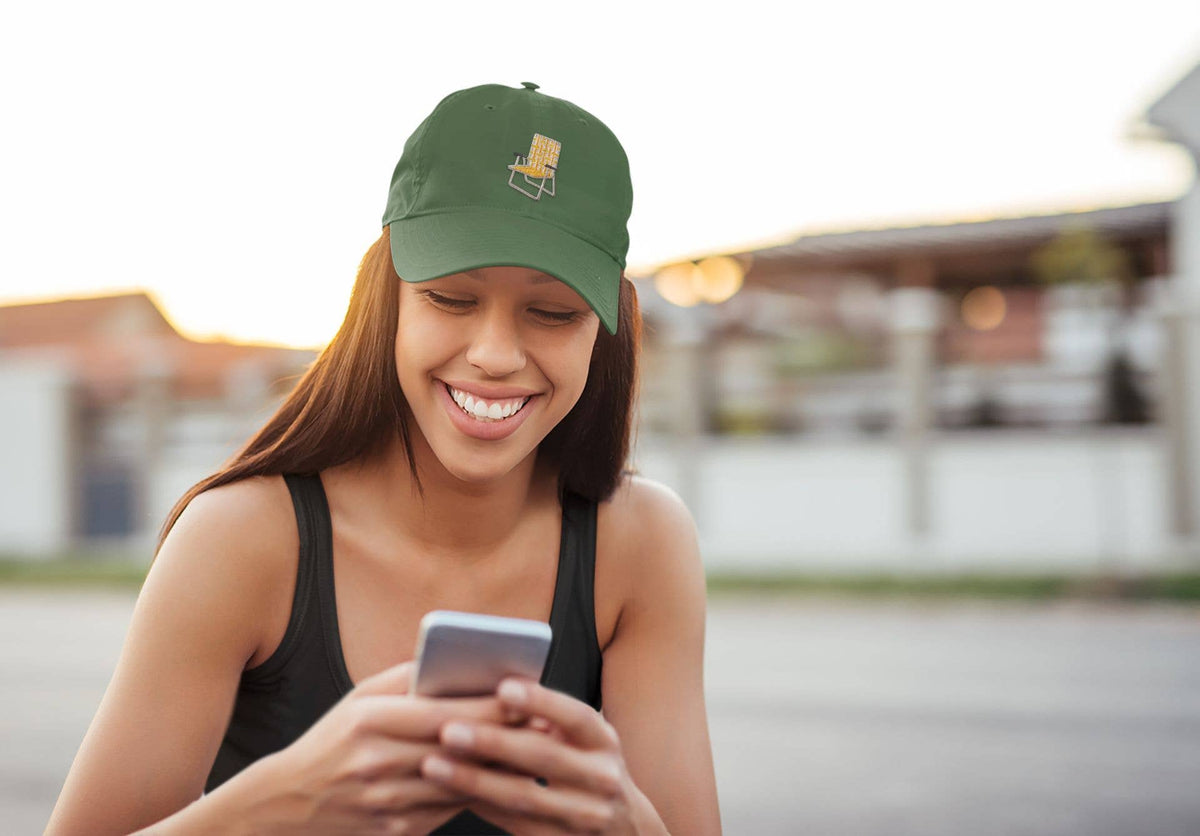 Person wearing a green cap with a yellow embroidered chair and black tank top, using a smartphone outdoors.