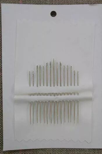 Set of needles in a white cardboard holder on a textured surface