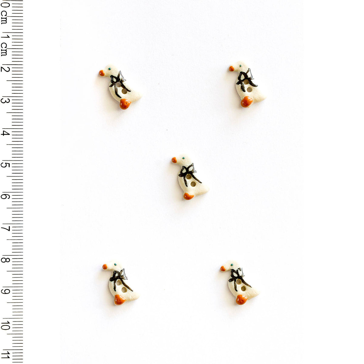 Five tiny geese-shaped buttons on a white background with a ruler for scale.