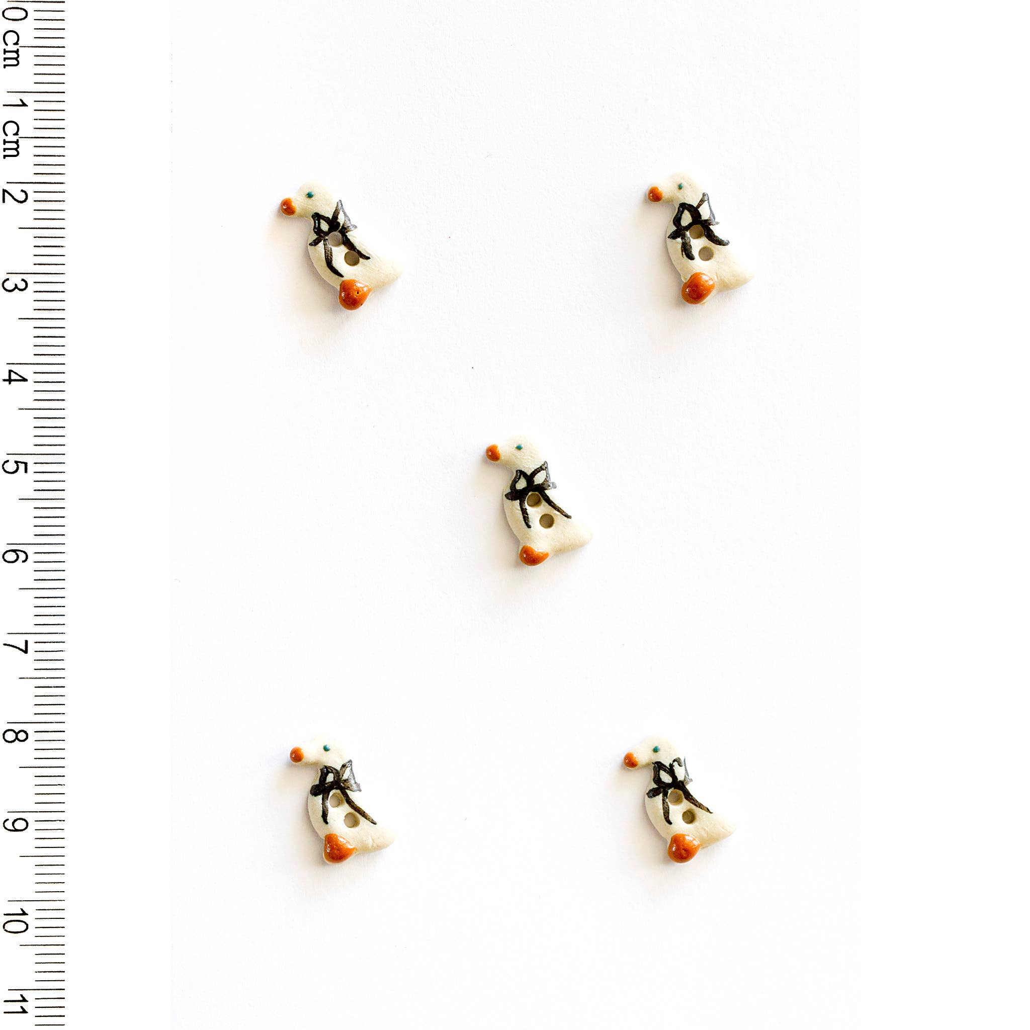 Five tiny geese-shaped buttons on a white background with a ruler for scale.