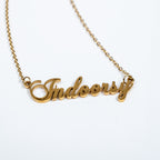 Gold necklace with 'Indoorsy' pendant on a white background