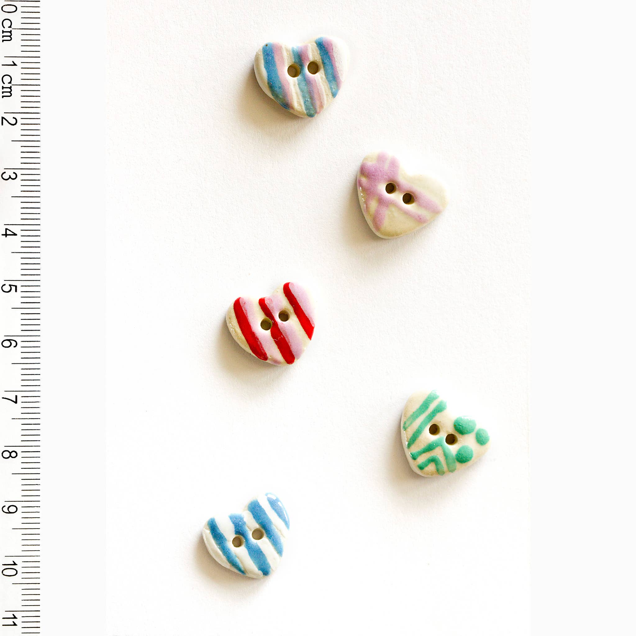 Colorful heart-shaped buttons on a white background with a ruler for scale.