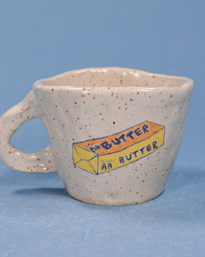 Speckled ceramic mug with a painted butter box design on a blue background
