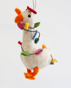 A white felt Christmas ornament shaped like a goose, decorated with orange felt beak and feet, a red felt hat, and colorful felt Christmas lights in green, blue, pink, yellow, and red, hanging against a plain white background.