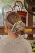 Person wearing a blue and yellow scrunchie in their hair, standing outdoors with a blurred background