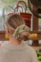 Person wearing a blue and yellow scrunchie in their hair, standing outdoors with a blurred background