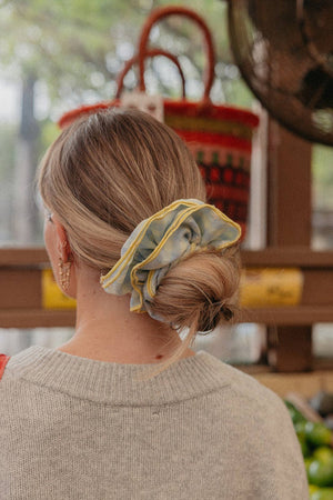 Person wearing a blue and yellow scrunchie in their hair, standing outdoors with a blurred background