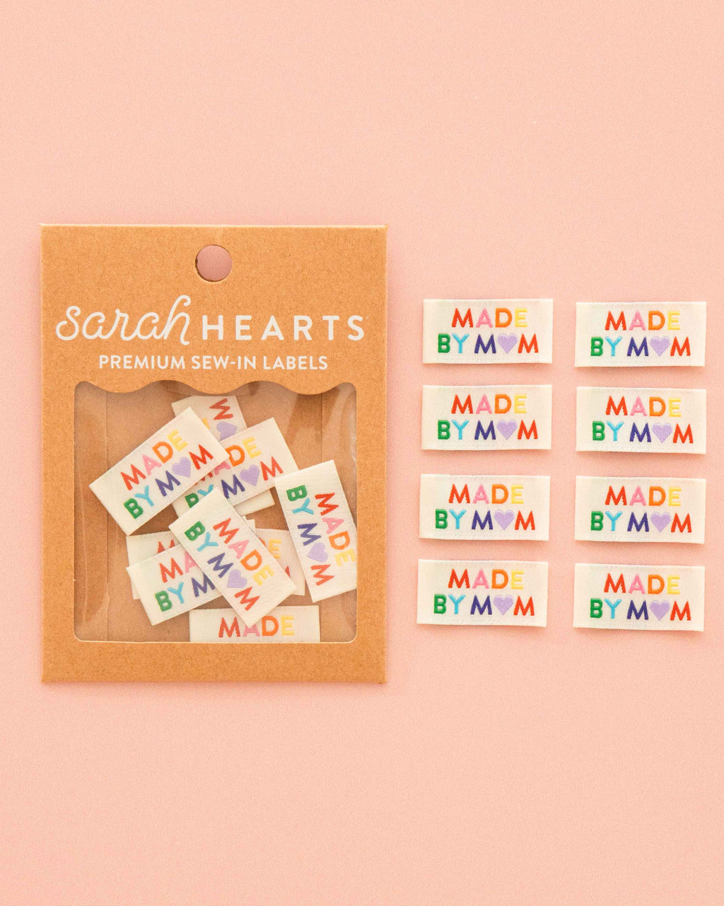 Sarah Hearts premium sew-in labels that read 'MADE BY MOM' in colorful lettering on a pale pink background.