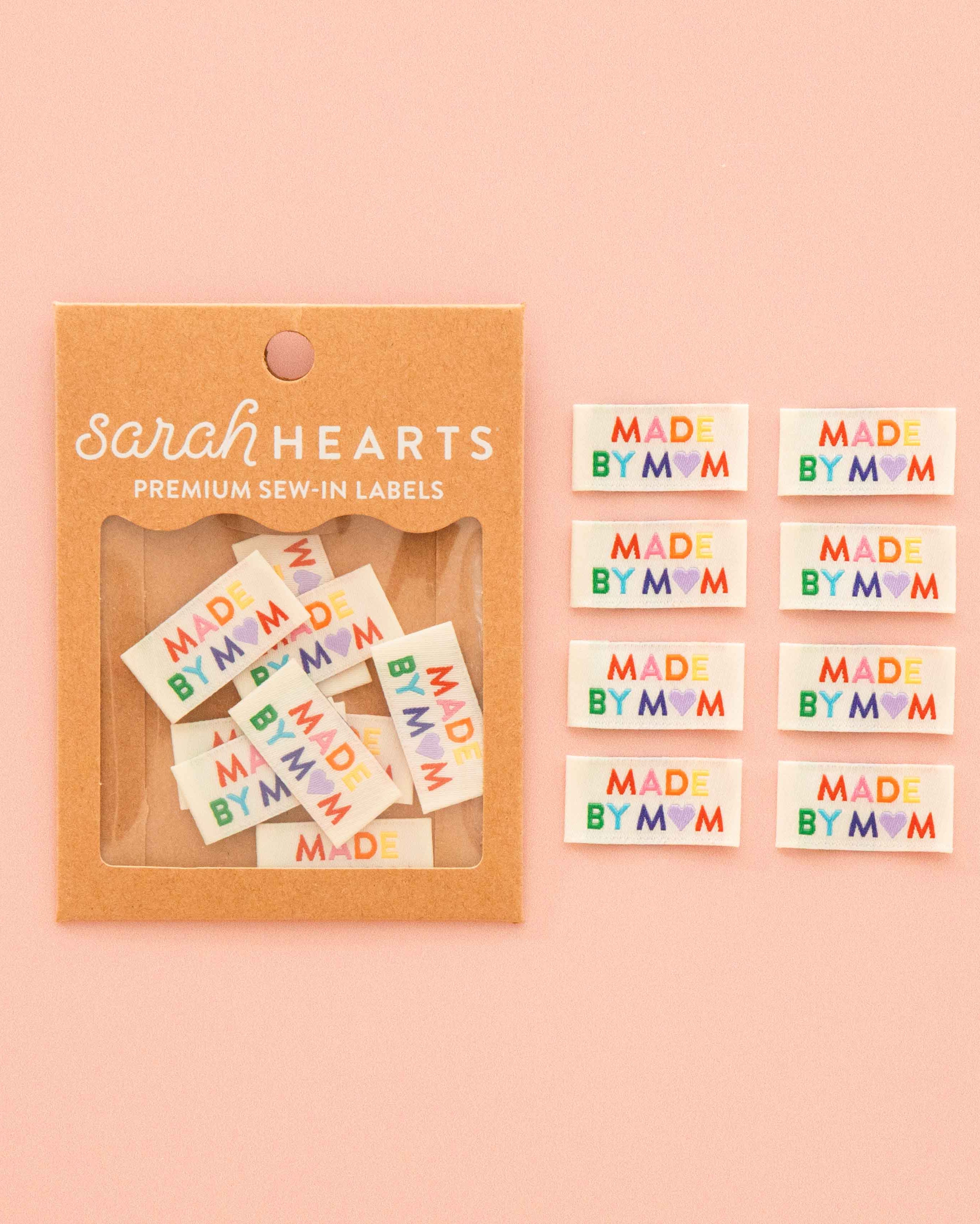 Sarah Hearts premium sew-in labels that read 'MADE BY MOM' in colorful lettering on a pale pink background.