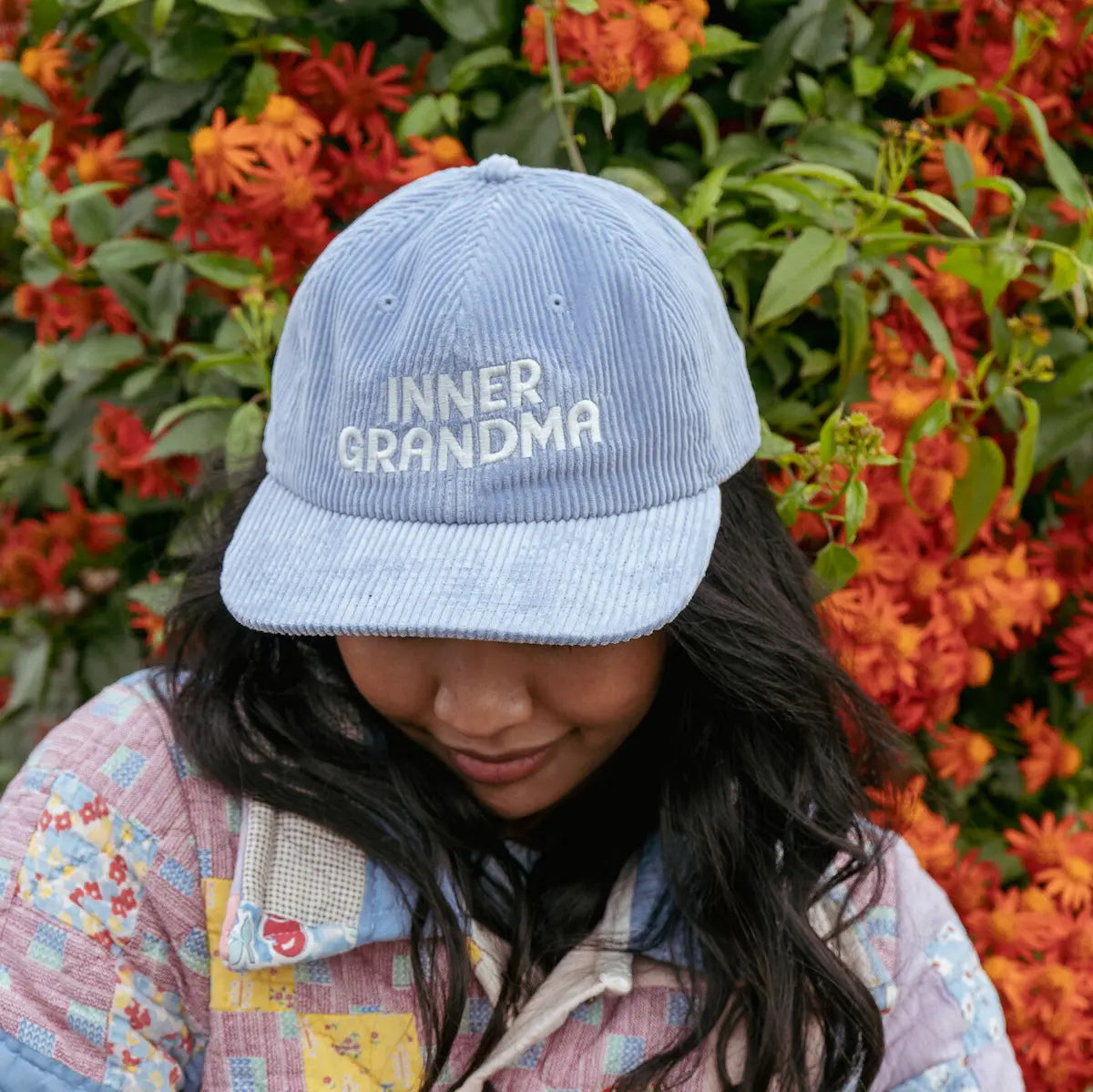 Person wearing a blue cap with 'INNER GRANDMA' text in front of orange flowers