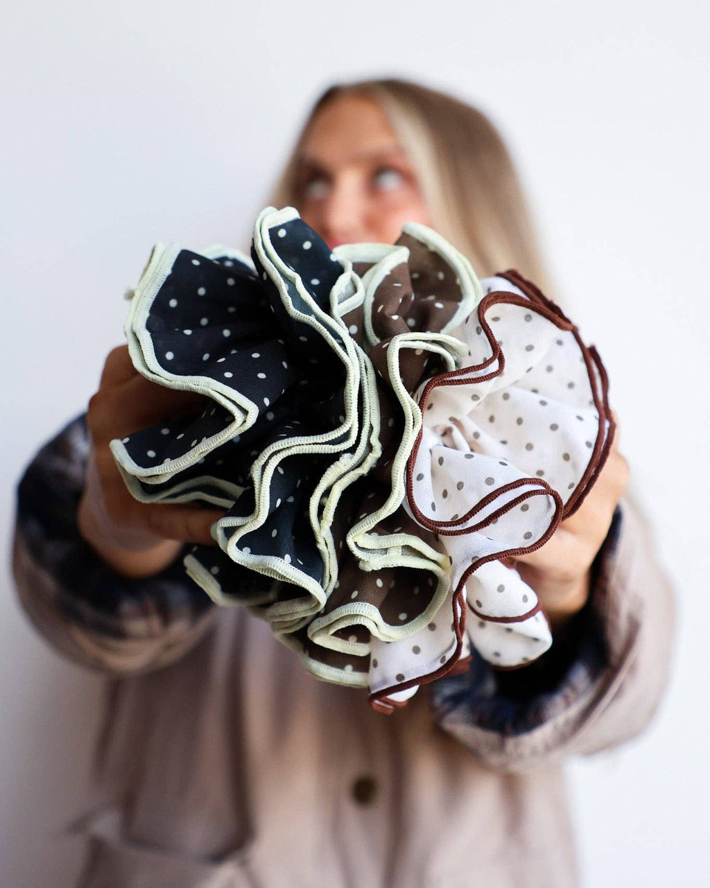 Person holding a group of scrunchies with various designs against a white background