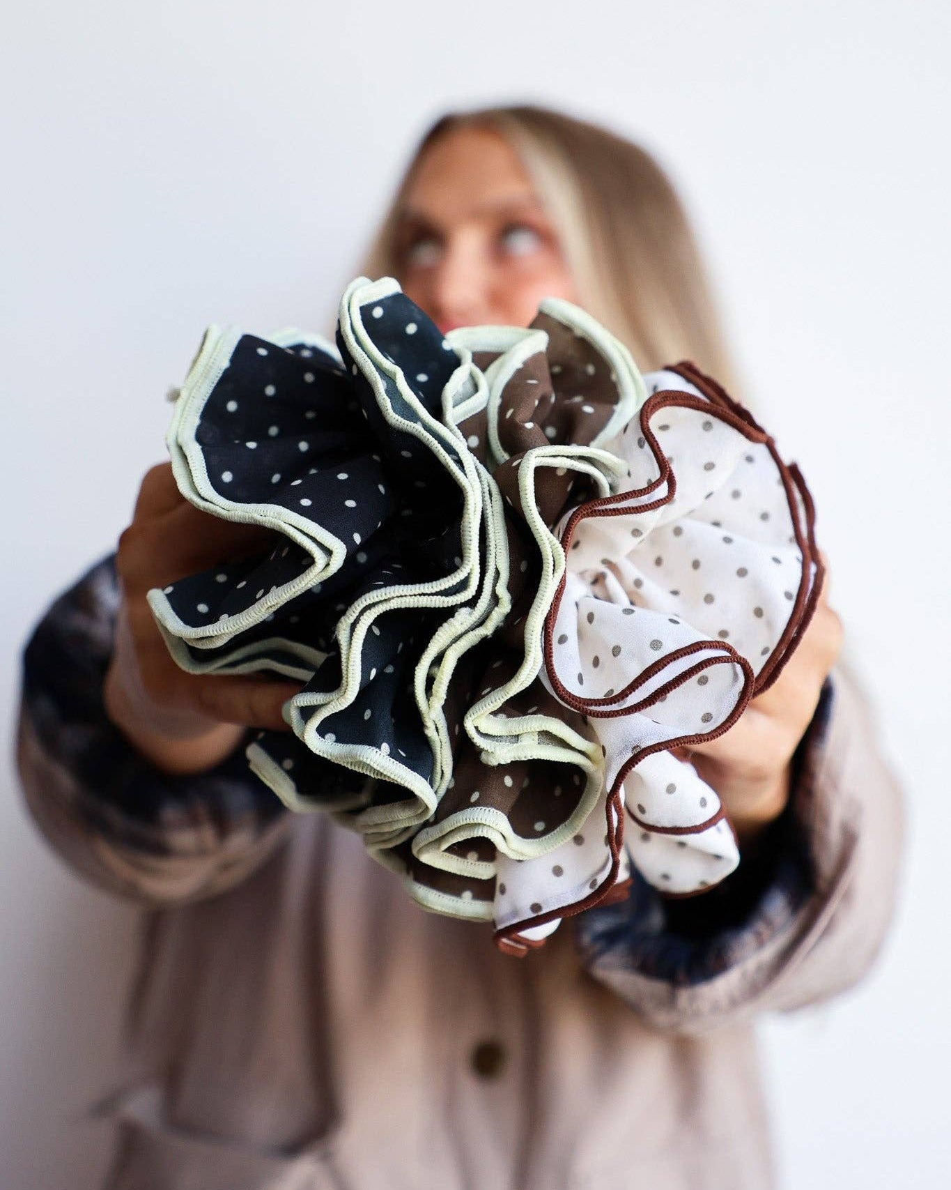 Person holding a group of scrunchies with various designs against a white background