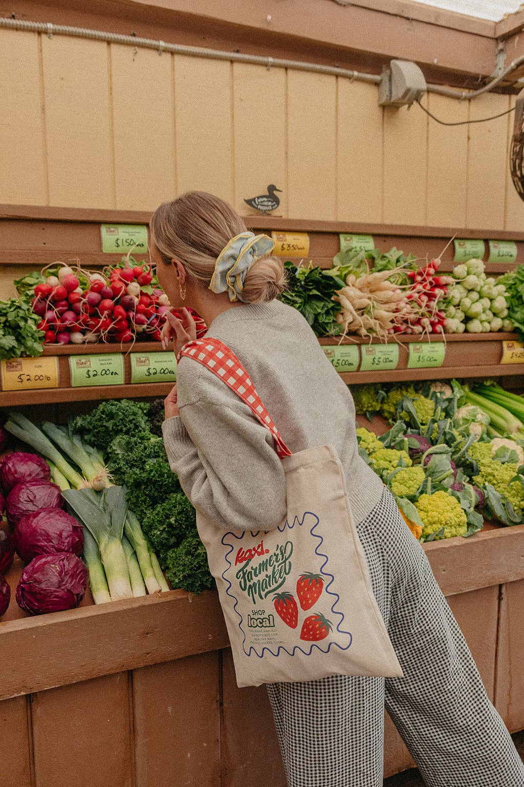 Person shopping at a farmers market wearing a blue and yellow scrunchie with a reusable bag.