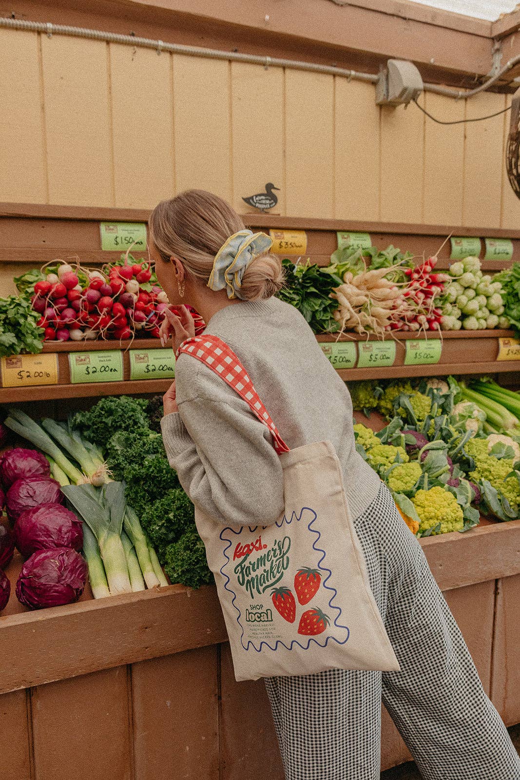Person shopping at a farmers market wearing a blue and yellow scrunchie with a reusable bag.