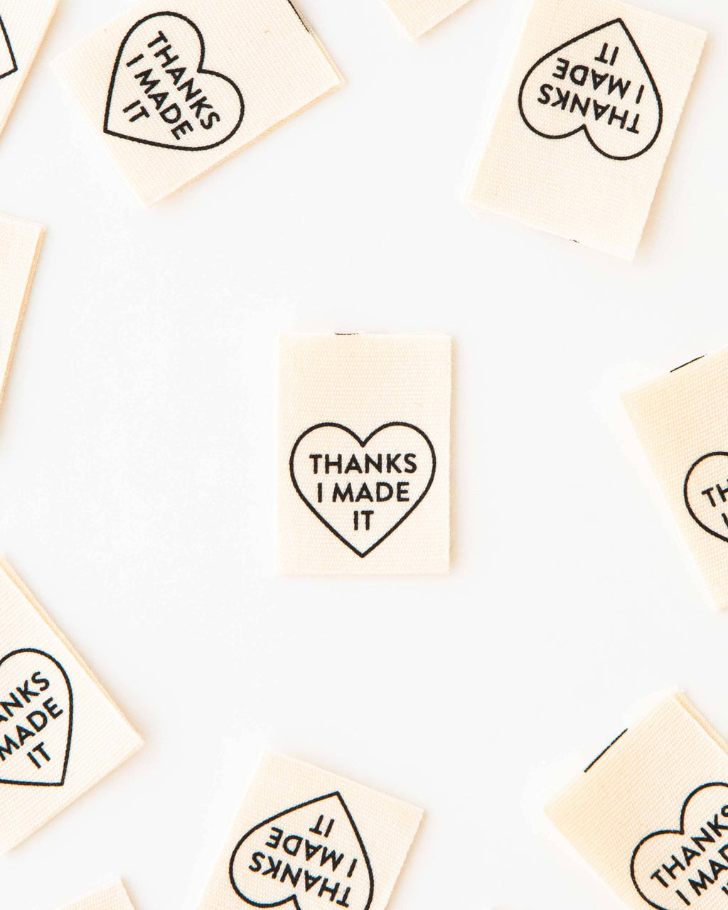 Small rectangular sew-in labels with heart-shaped text 'THANKS I MADE IT' arranged on a white background.
